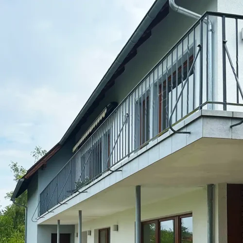 Blick von unten zum Balkon nach Balkonsanierung: Metallgeländer, neue hellgraue Fliesen an der Kante