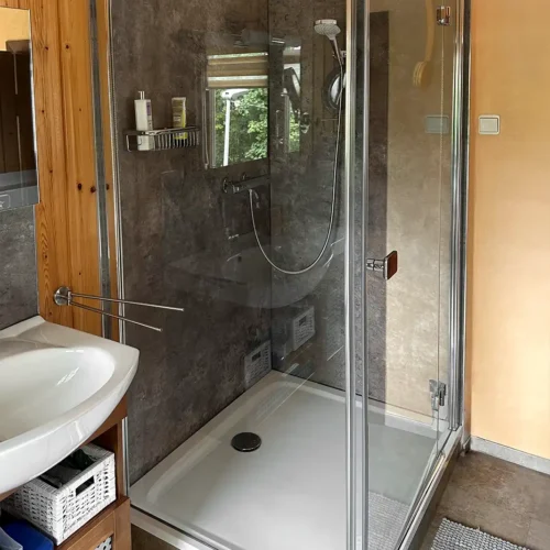 Dusche in Ecke neben Waschbecken mit dunkelbrauner fugenloser Rückwand